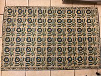 Full view of the rectangular vintage needlepoint rug showing the repeating floral grid pattern with blue and green motifs on a beige background.