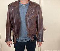 Front view of brown vintage leather jacket worn by a model, showing zipper, collar, pockets and belt.