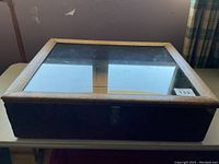 Front view of the rectangular wooden display case with a clear glass top, resting on a table.