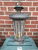 Full view of weathered antique brass lantern showing patina and clear etched glass panels with candle inside.