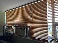 Image of wood blinds covering large windows with some furniture visible nearby.