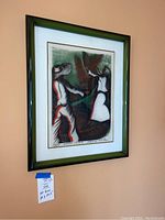 Frontal photo of Brazilian art print with black and green ombré frame hung on peach wall, showing abstract figures.