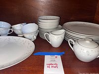 Assorted Japanese china with stacked dinner plates, salad plates, teacups, creamer and sugar bowl on wooden shelf.