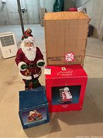 Photo showing large ceramic Santa figure with traditional red attire and holly on hat, boxed Lifetime Santa candle, boxed ceramic Santa box in blue box, and large fragile cardboard box.