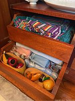 Drawer with colorful ceramic napkin holders shaped like red apples, green pears, and orange pumpkins, alongside additional linens and fabric pieces folded underneath.