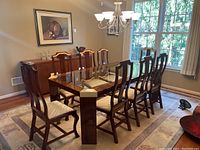 View of the full dining table with eight chairs around it in a dining room with large window and chandelier overhead.