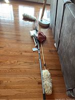Photo showing two extension rods laying on wooden floor, one with white fluffy duster, the other with a duster and red cloth