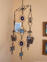 Full view of the Latin American copper and stoneware hanging mobile suspended on a wall corner, showing the overall shape, copper wirework, and blue/turquoise medallions.