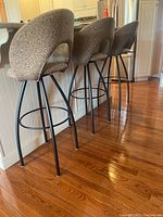 Side view of four bar stools lined up along a kitchen counter, showing the full height and design with black metal legs and upholstered seats and backs.