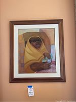 Full view of the framed painting showing the woman wrapped in a yellow shawl holding a flower, hanging on a wall.