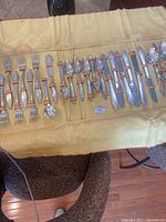 Overall view of the silver-plated flatware laid out on a yellow cloth case, showing forks, knives, spoons, and serving utensils secured with orange loops
