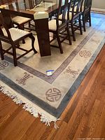 Full view of the wool area rug under dining table showing cream, taupe, and soft blue colors with Asian motifs and fringe tassels.