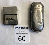 Front view of two metal vesta match safe cases showing wear and embossed design on one.