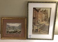 Photo showing both framed watercolour paintings side by side; one small landscape of Welsh mountains, larger street scene with church tower.