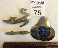 Three brooches shown front view with ruler for size reference.