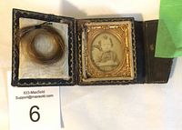 Open satchel case showing the coiled lock of child's hair on left and the oval framed daguerreotype or ambrotype photo of young girl on right.