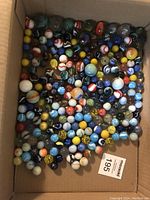 Box filled with assorted marbles in various sizes and colors showing diverse patterns and finishes.