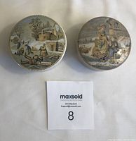 Top view of two Prattware jars with lids showing different winter-themed scenes on lids.