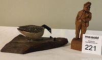 Photo of both wood carvings side by side: a Canada goose on a wood base and a man figure carved from wood