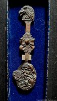 Close-up of the front of the 1990 Harley Davidson pewter collector spoon featuring Santa Claus and Christmas imagery with an eagle head handle, displayed in blue velvet gift box.