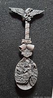 Front of pewter collector spoon showing eagle, bow with bells, Harley Davidson logo, and detailed motorcycle scene on bowl.