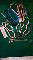 Full layout of vintage jewelry lot including necklaces, chokers, earrings, and bangles in various bead and shell styles on green background.