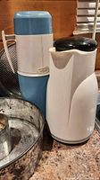 Blue and white thermos and white coffee jug with black lid on countertop with springform pans visible
