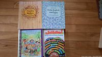 Photo of 5 music books arranged on wooden floor: Country Western Hits, Family Scrapbook Faith and Joy, Children's Song Classics spiral book, and 2 other music books.