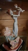 Side view of Natelia Collection mother lifting baby figurine near crib base with fabric detail