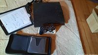 Full view of the PlayStation 3 console, controller, cords, pad protector and CD/DVD pouch on beige rug
