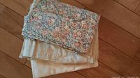 Stack of three cotton quilting fabrics with floral, solid beige, and leaf pattern visible, on wooden floor