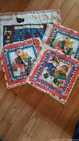 Four square pillow tops and one rectangular door stocking quilted panel arranged on wood floor, designs featuring children, animals, and houses.