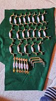 Full set of cabinet hardware pieces arranged on green fabric, showing 20 brass and ceramic curved pulls, plus 9 other pulls.