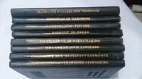 Stack of eight hardcover dressmaking instruction books showing spines with gold lettering.
