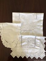 Three antique Irish linen pieces laid out on a dark wood surface showing detailed embroidery, lace, and cutwork designs.