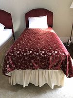 Twin bed with burgundy duvet cover featuring gold floral vine pattern and cream skirt.