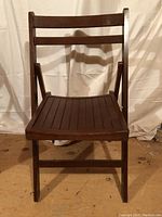 Single folding wooden chair facing front showing slatted seat and backrest, dark wood finish.