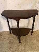 Photo of the wooden side table featuring a scalloped rectangular top, spindle legs, and a lower shelf. The wood is dark-stained, and the table shows wear and indications it needs some TLC on the top surface.