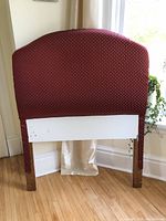 Front view of one burgundy upholstered twin headboard with gold diamond pattern, showing full fabric and wooden legs with hardware