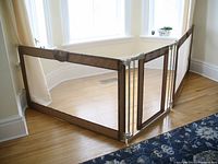 Gate installed in a corner with three panels arranged in an L shape across a windowed area, showing brown fabric and mesh construction.