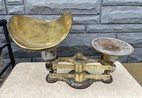 Front view of antique balance scale showing the brass concave pan on the left and flat weighing plate on the right, with measurement arms and base visible.