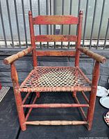 Front view of the antique Canadian primitive armchair with red paint and wicker seat showing some wear.