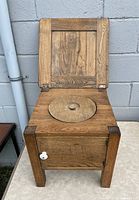 Front view of antique pine commode chair with hinged lid open showing circular seat cover.
