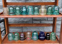Full view of 18 antique glass and porcelain insulators on wooden shelf, front view showing various colors and designs