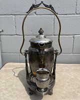 Front full view of silverplated tilting water pitcher with attached stand and tumbler showing overall condition and design.