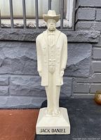 Full frontal photo of the off-white plaster statue standing on a base labeled 'JACK DANIEL'.
