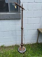 Full height view of the vintage oak floor lamp showing the carved spindle shaft standing against an exterior block wall. Lamp base is round with a slightly raised edge.