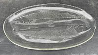 Top-down view of clear glass oval platter with two embossed fish designs.