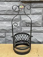 Front view of the black wrought iron tilting liquor holder with visible circular base and Grand Marnier enamel crest on top center.