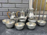 Front view of the complete pewter set showing various bowls, pitchers, teapots and cups with hammered texture